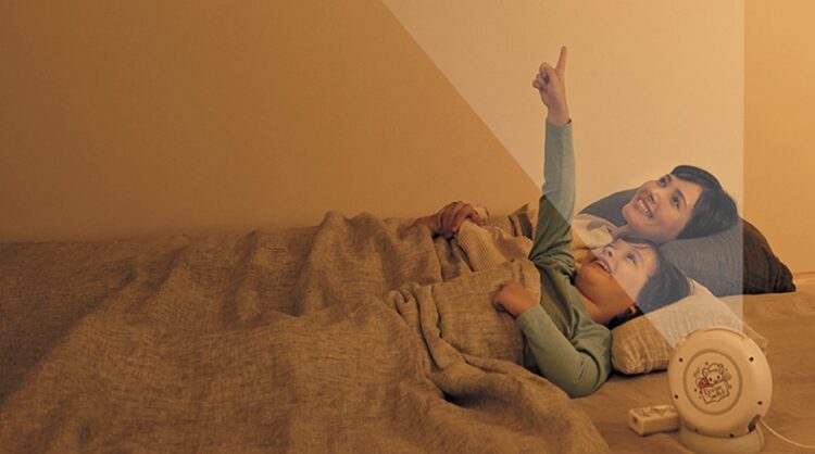 サンリオイングリッシュマスターのプロジェクター機能で、親子が寝転びながら天井に映し出された映像を楽しんでいる様子。リラックスした雰囲気の中で自然に英語に触れられるのが魅力です。