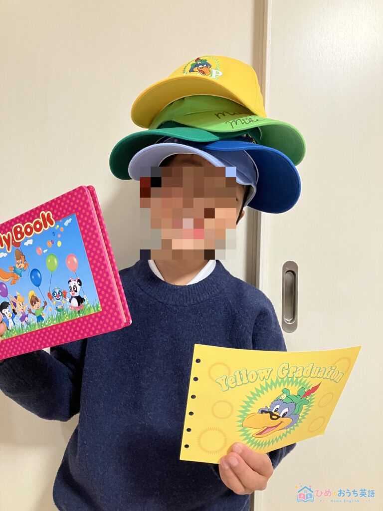 DWEの黄色卒業帽を重ねて被りMy Bookとイエローグラデュエーションの賞状を持つ息子(顔はモザイク処理)